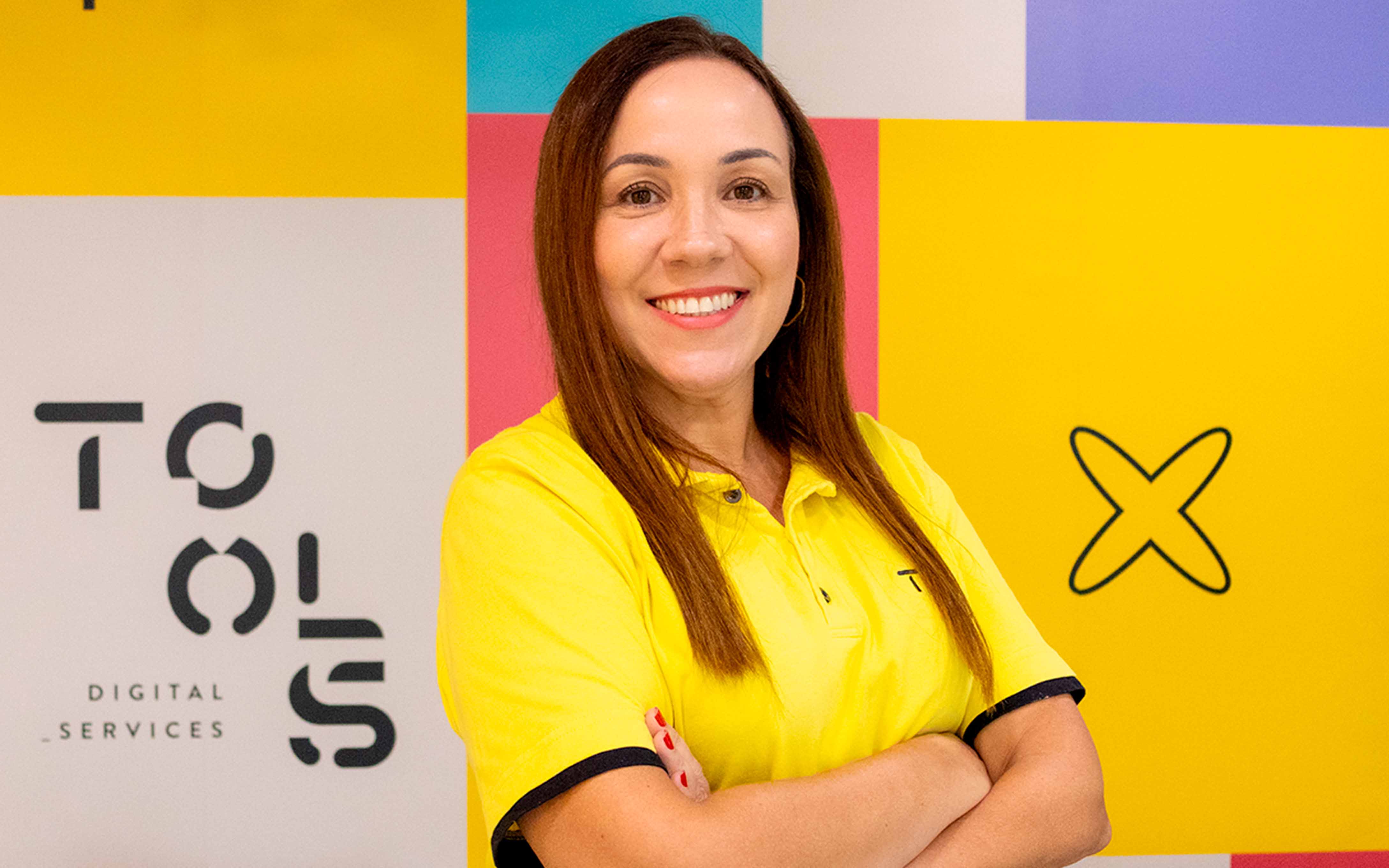 Mulher branca de cabelo castanhos longos, sorrindo utilizando camiseta polo amarela da TOOLS Digital Services.