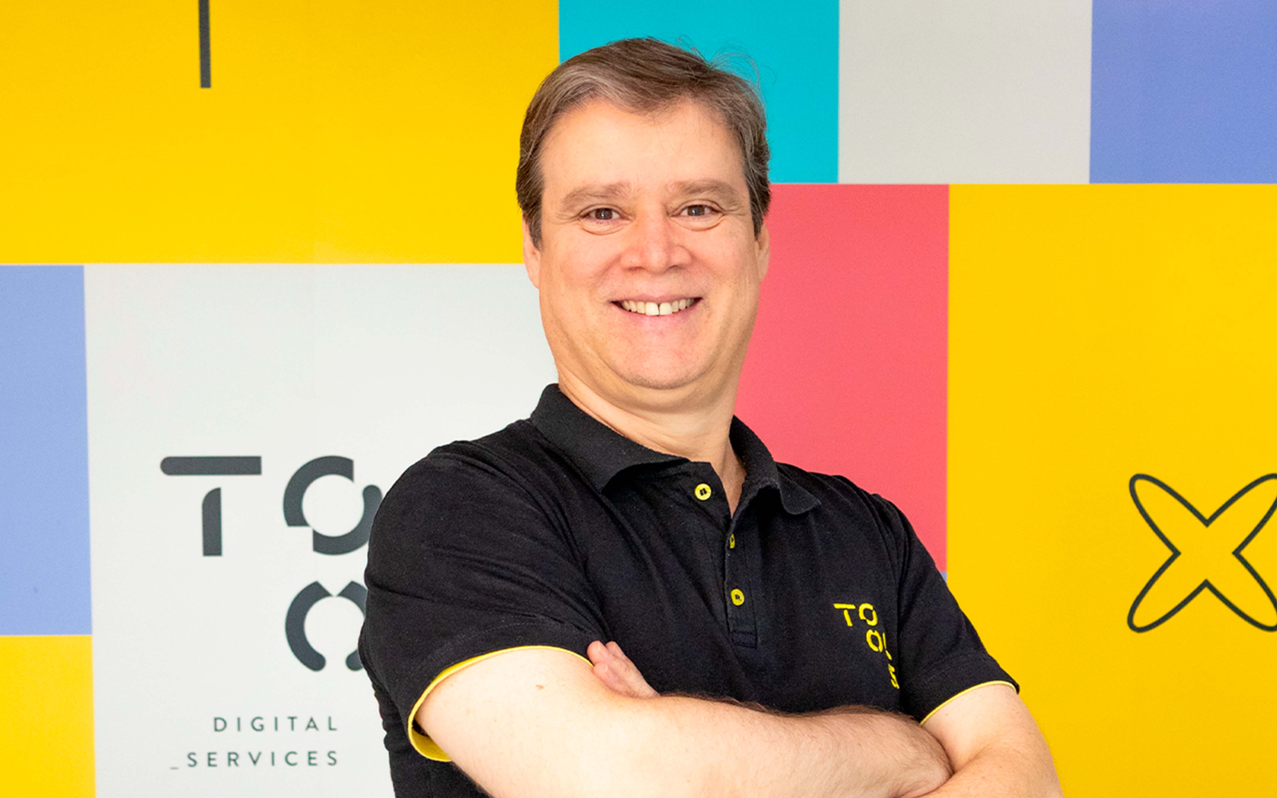 Homem branco de cabelos curtos e grisalhos, sorrindo utilizando camiseta polo preta da TOOLS Digital Services.