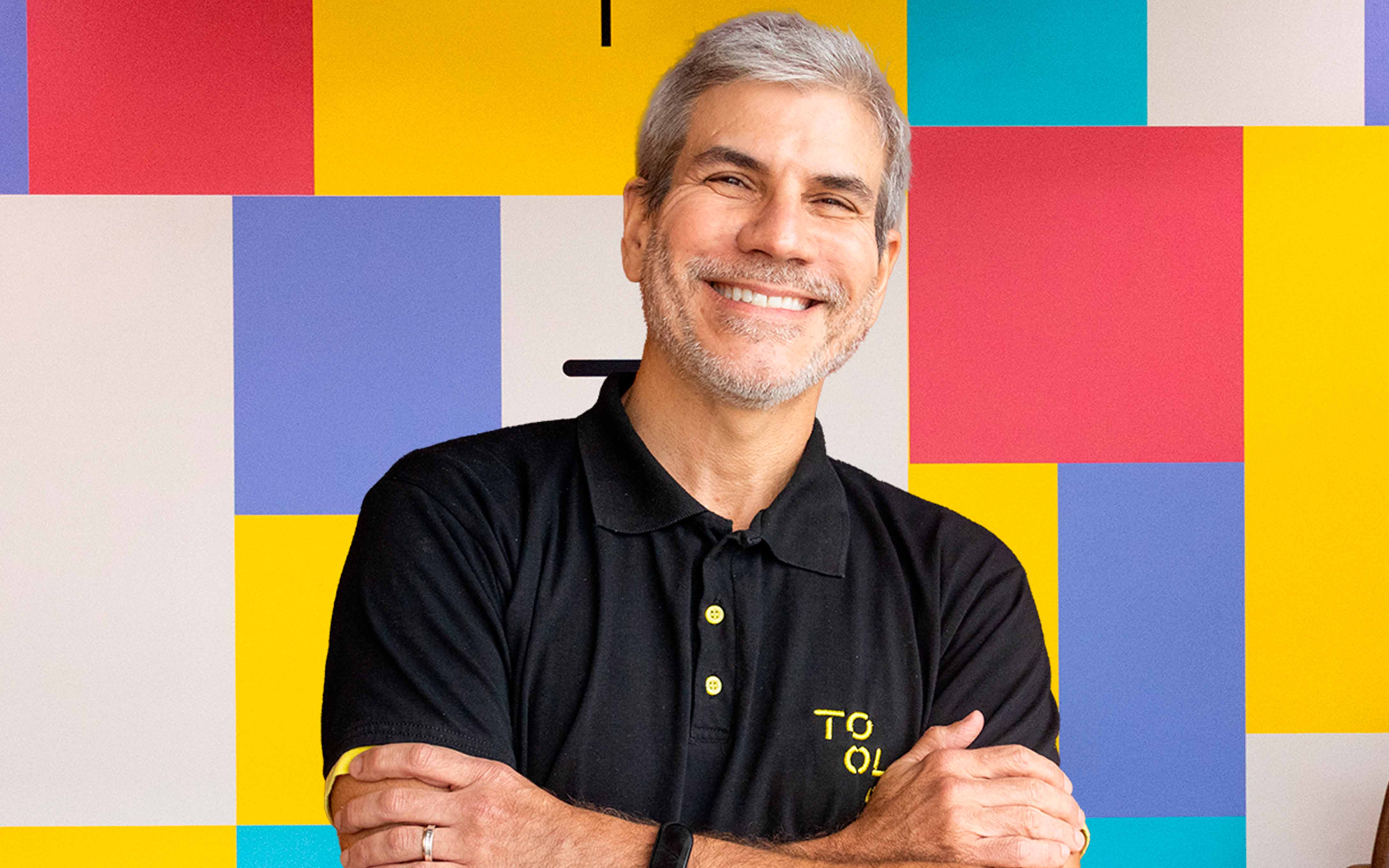 Homem branco de cabelo grisalho, sorrindo e utilizando camiseta polo preta da TOOLS Digital Services.