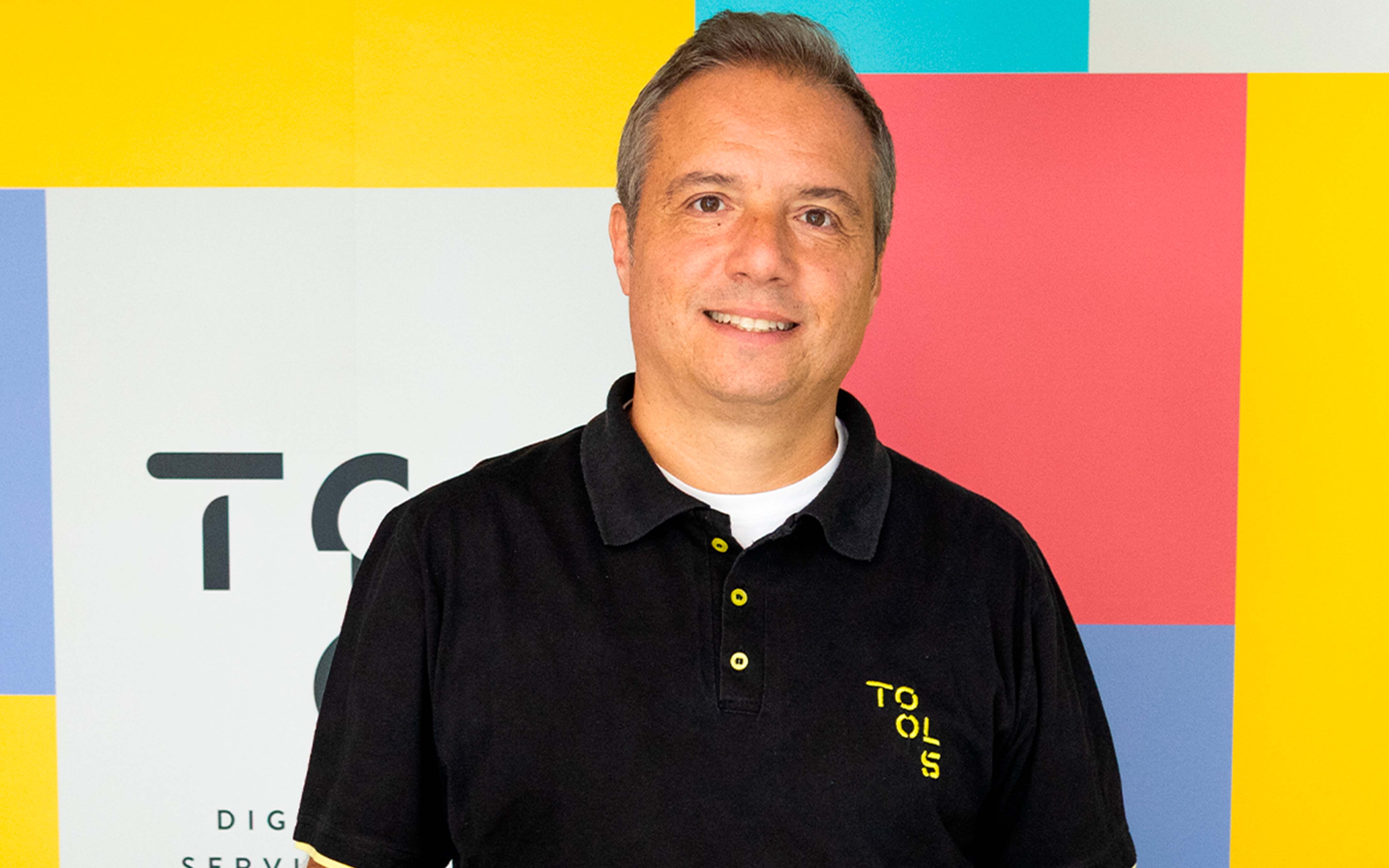 Homem branco de cabelo grisalho, sorrindo e utilizando camiseta polo preta da TOOLS Digital Services.