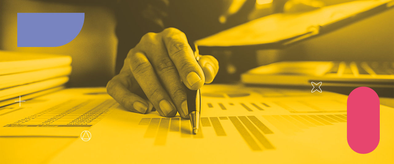 Uma mão segurando uma caneta que está apontando para um gráfico no papel.